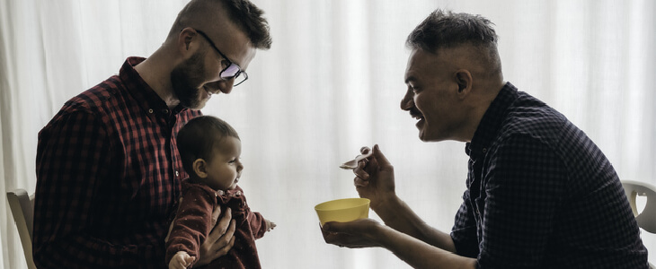Married LGBTQ couple feeding food to their baby son