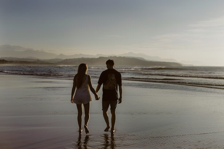 young couple walks along beach at sunset holding hands