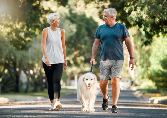 A retired couple walking their dog in the park.