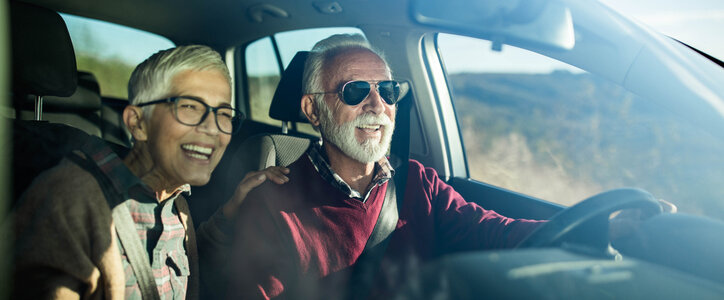 Retired, middle-aged couple driving a car down the road.