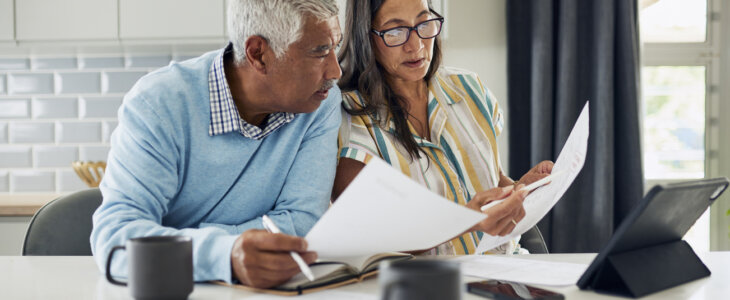 An older couple is sitting at their kitchen table reviewing financial documents.