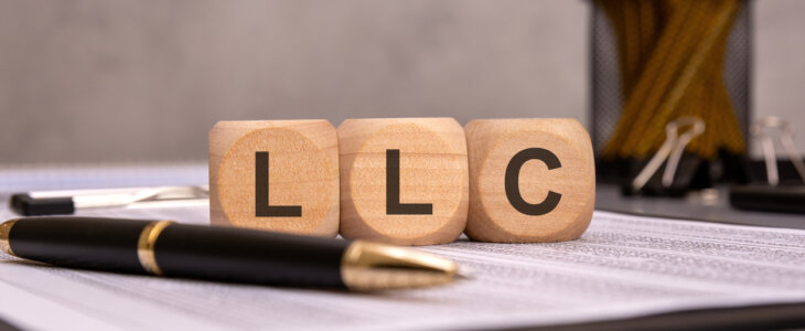 wooden cubes displaying the abbreviation LLC on a work desk with financial documents, a pen, and office supplies. the image represents limited liability company concepts, business structures, and legal entities