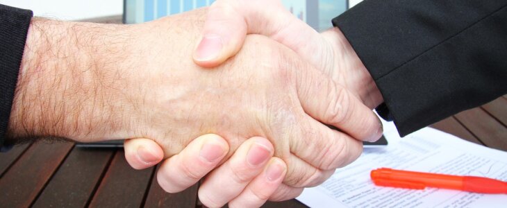 Business partners shaking hands over legal documents, symbolizing business succession planning and ownership transition.