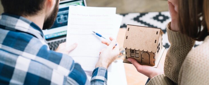 Couple reviewing legal documents while holding a model house, symbolizing divorce settlement, property division, and financial planning.